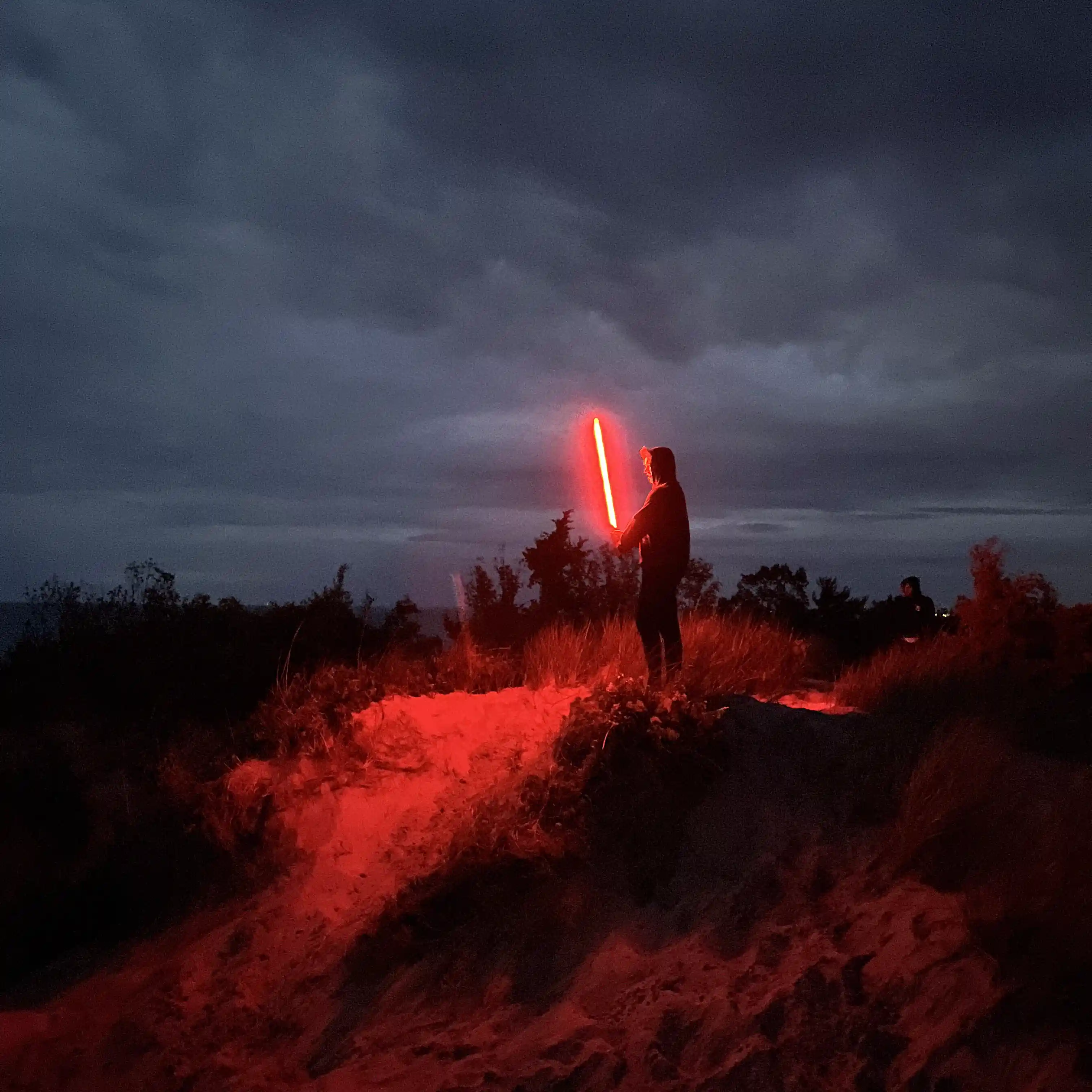 man on a dune holding a red lightsaber